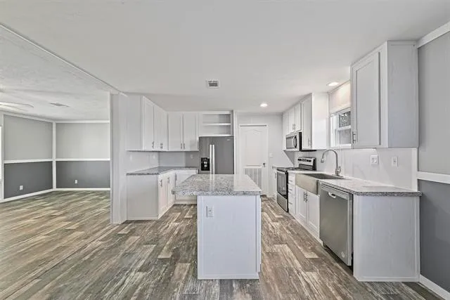 a living room with stainless steel appliances kitchen island granite countertop a sink a stove a refrigerator and white cabinets