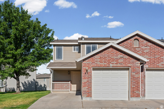 652 West 800 North, Unit 45 Clinton, UT 84015 - Photo 1 of 17 Brick and siding exterior featuring an attached garage, covered front porch with white railing, and a mature tree