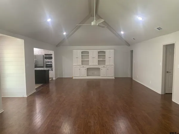 an empty room with wooden floor kitchen view and a window