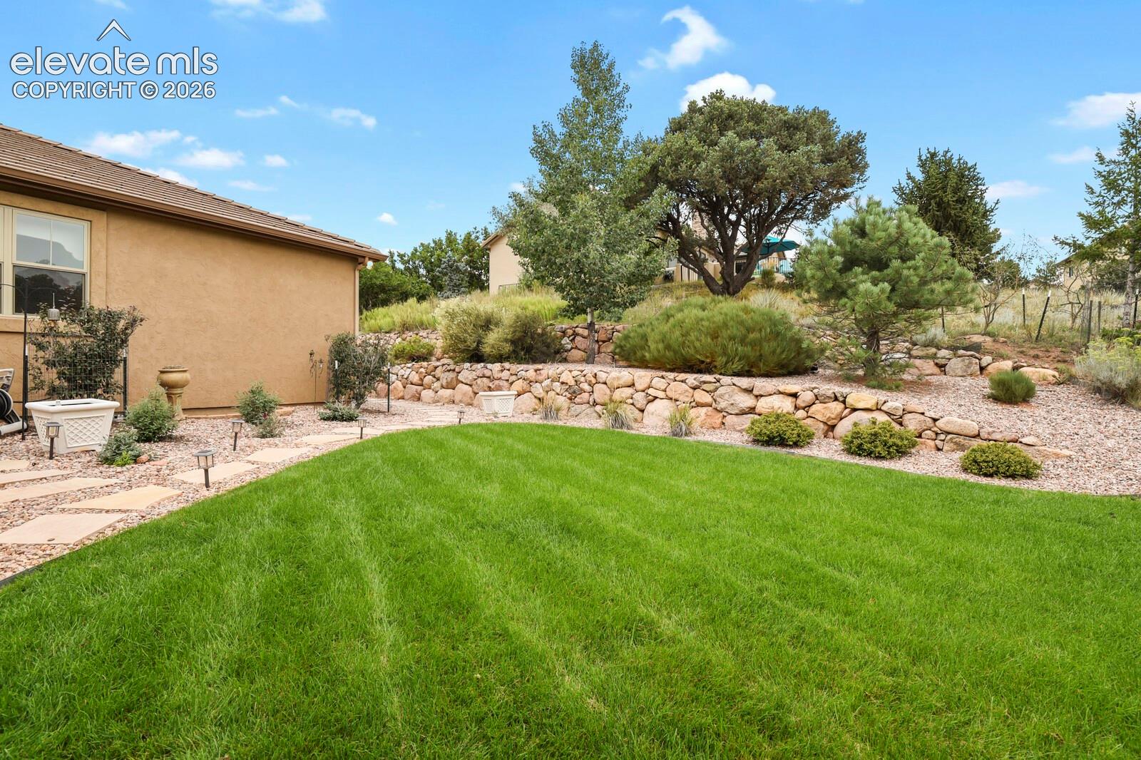 5545 Wilson Road Colorado Springs, CO 80919 - Photo 38 of 48 Lawn area with a stone paver pathway, terraced landscaping featuring natural stone retaining walls, and mature trees and shrubs