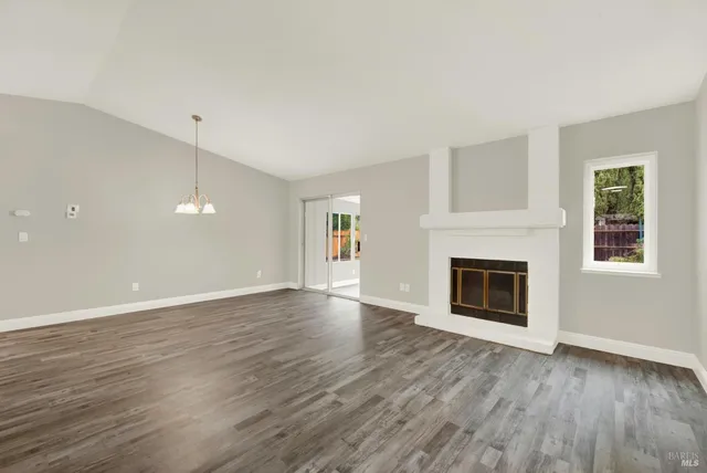 a view of an empty room with wooden floor fireplace and a window