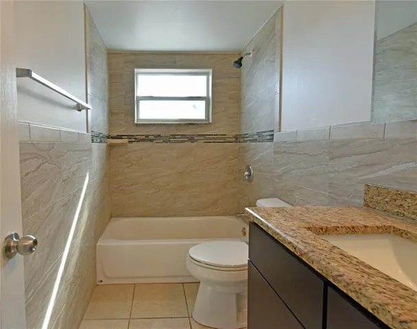 a bathroom with a granite countertop bathtub shower sink vanity and toilet
