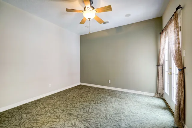 an empty room with a chandelier fan and windows