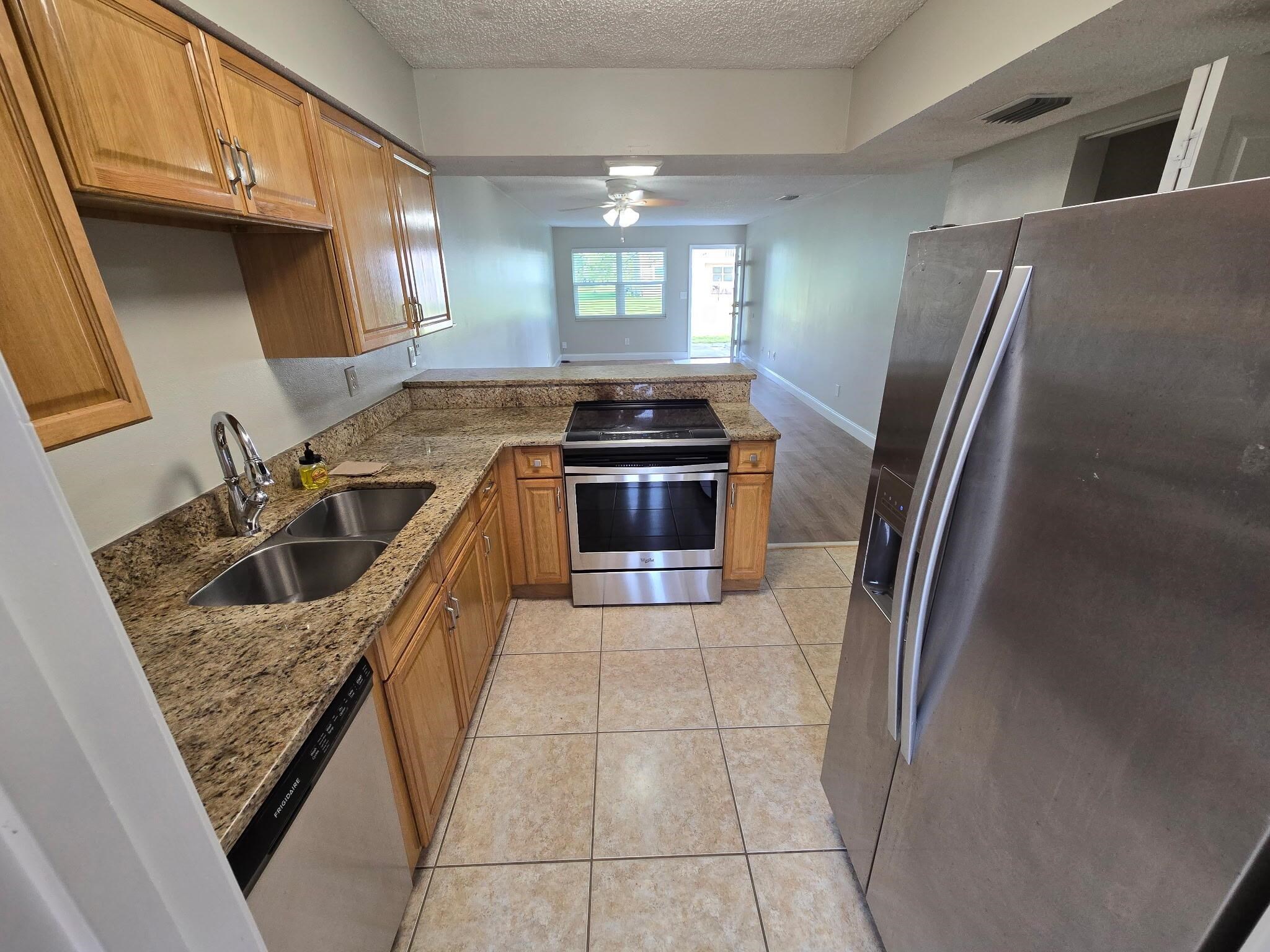 125 Rio Del Mar Street, Unit B St. Augustine, FL 32080 - Photo 4 of 17 Kitchen with stainless steel appliances, wood finish cabinetry, dark stone countertops, a ceiling fan, and a textured ceiling