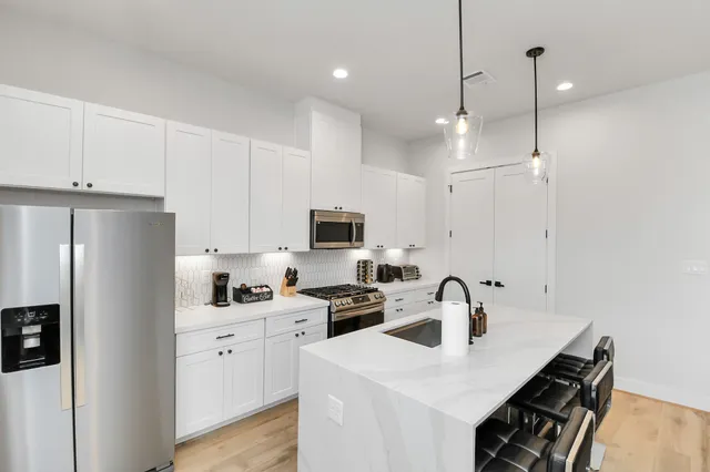 a kitchen with stainless steel appliances a sink a stove a refrigerator a center island and cabinets