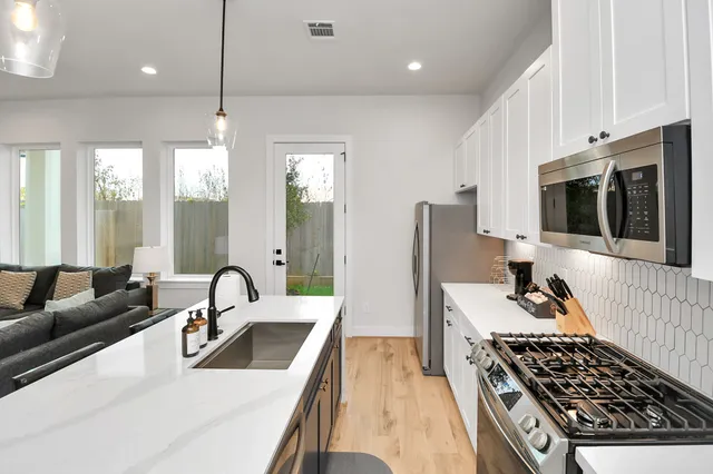 a kitchen with stainless steel appliances a stove a sink a refrigerator white cabinets and a dining table with wooden floor