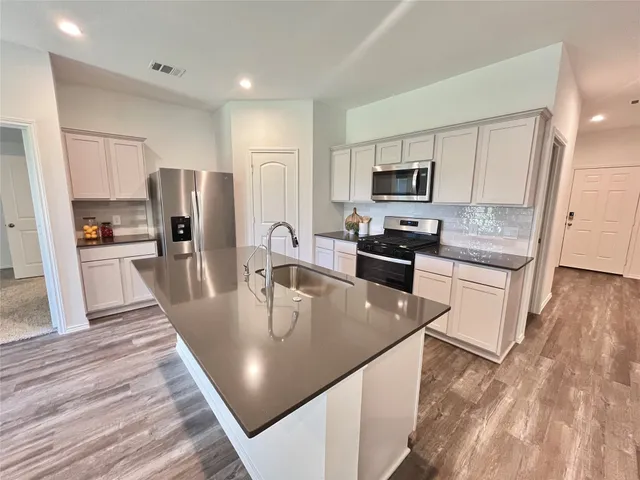 a kitchen with stainless steel appliances granite countertop a refrigerator a stove top oven a sink counter space and wooden floor