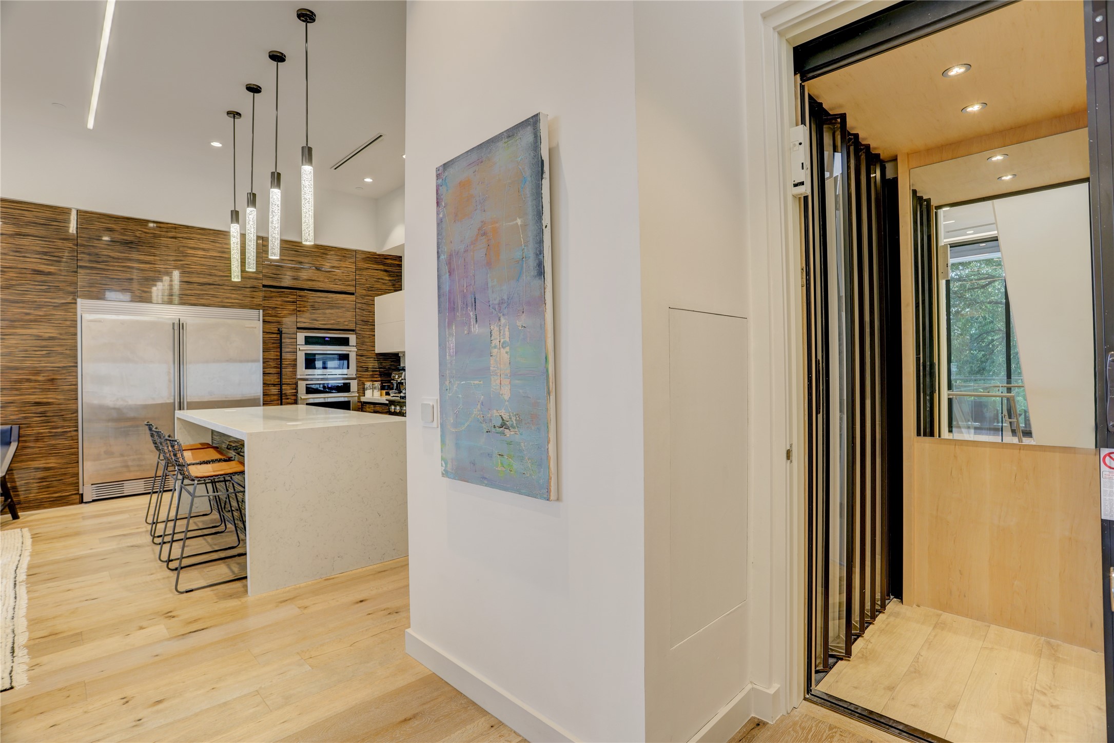 1807 Indiana Street Houston, TX 77006 - Photo 5 of 35 Elevator & Kitchen: Private home elevator opens directly onto the second-floor main living area, featuring a gourmet kitchen with a quartz waterfall island, designer cylinder pendant lights, and Electrolux ICON integrated appliances.