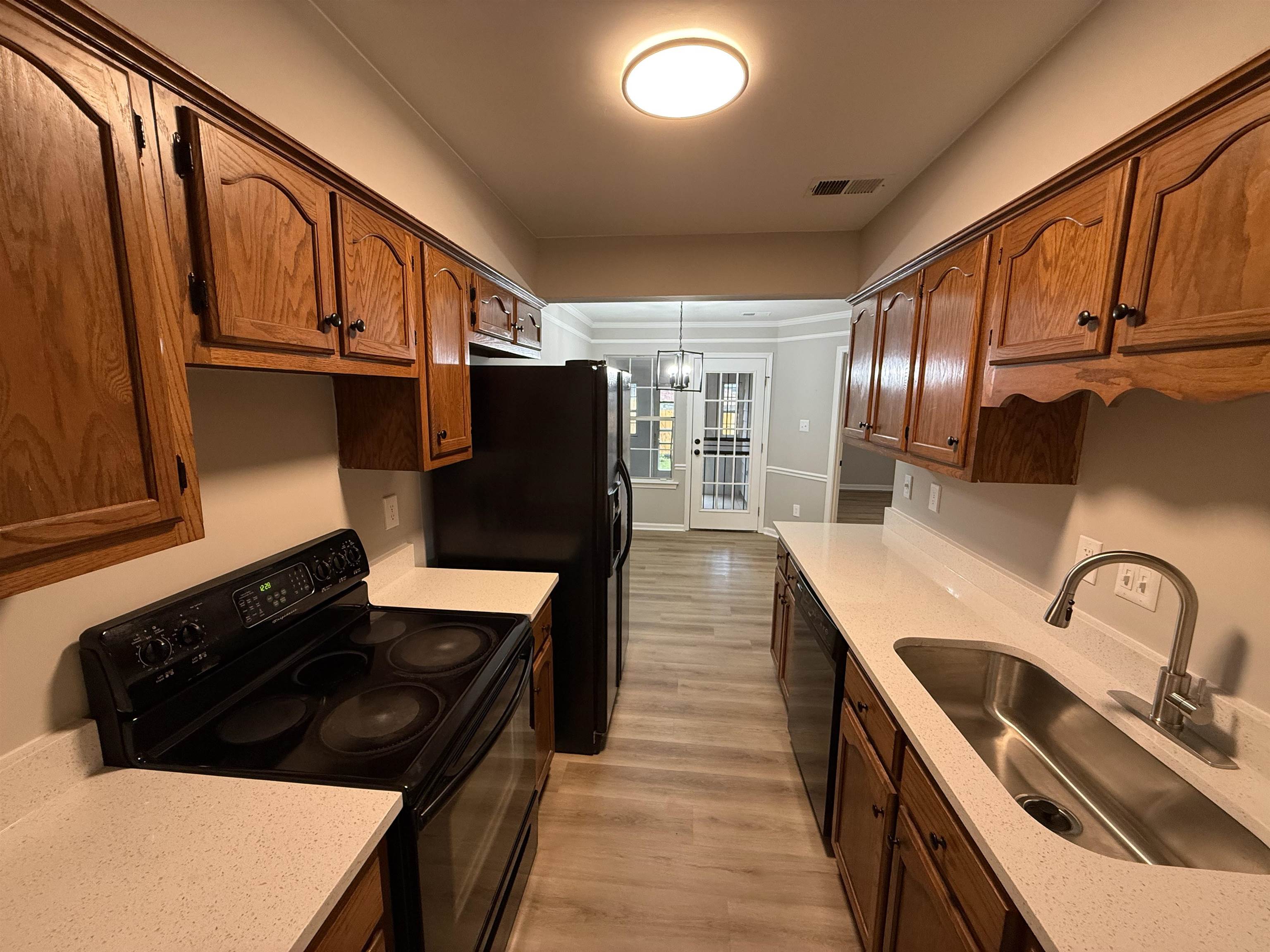 6913 Snyder Road Memphis, TN 38141 - Photo 3 of 20 Galley kitchen featuring wood cabinetry, light-toned countertops, and a full suite of black appliances