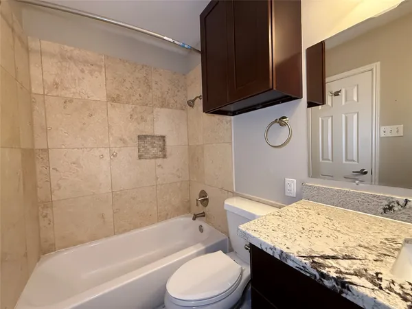 a bathroom with a granite countertop bathtub shower sink vanity mirror and toilet