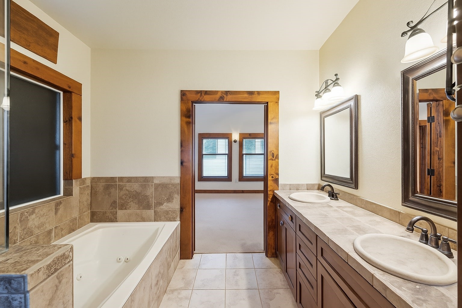 40570 Wildlife Run Hempstead, TX 77445 - Photo 16 of 43 Unwind in this spa-style bathroom featuring a jetted tub, dual vanities with stone counters, and warm wood accents. The open doorway leads directly back into the relaxing primary bedroom, seamlessly connecting comfort and luxury.