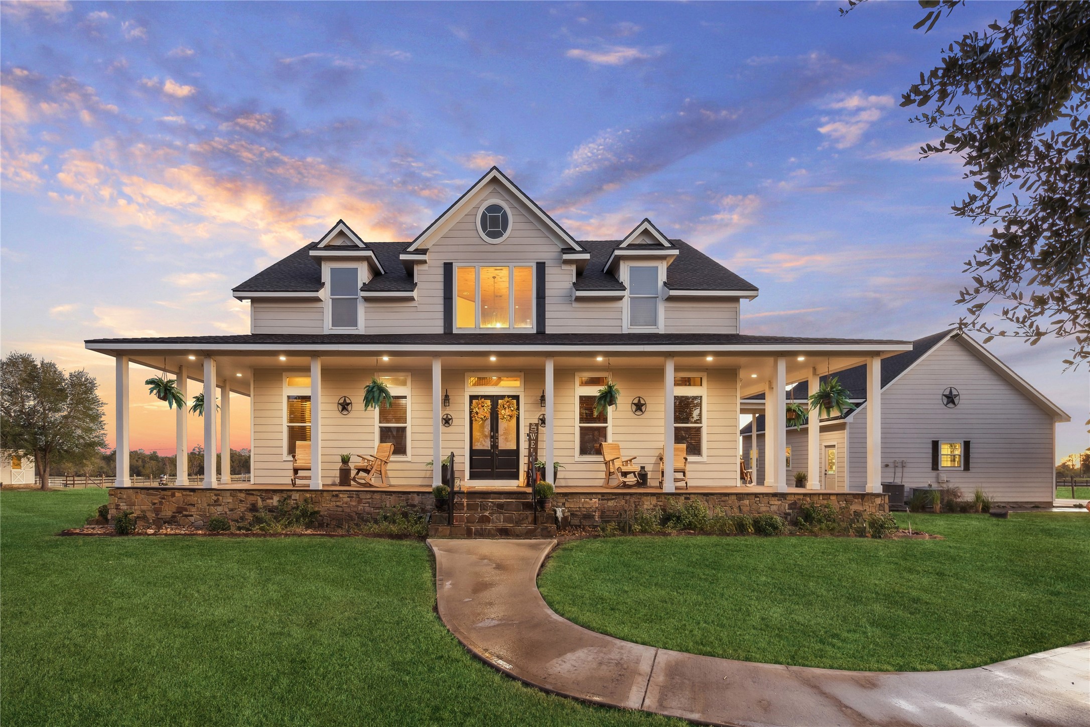 40570 Wildlife Run Hempstead, TX 77445 - Photo 2 of 43 Classic southern charm meets upscale country living in this stunning front elevation. The wraparound porch, dormer windows, and warm interior glow set a welcoming tone, while evening skies and lush green lawns frame the home like a storybook scene. The surrounding land enhances the lifestyle both visually and practically with a wildlife exemption in place.
