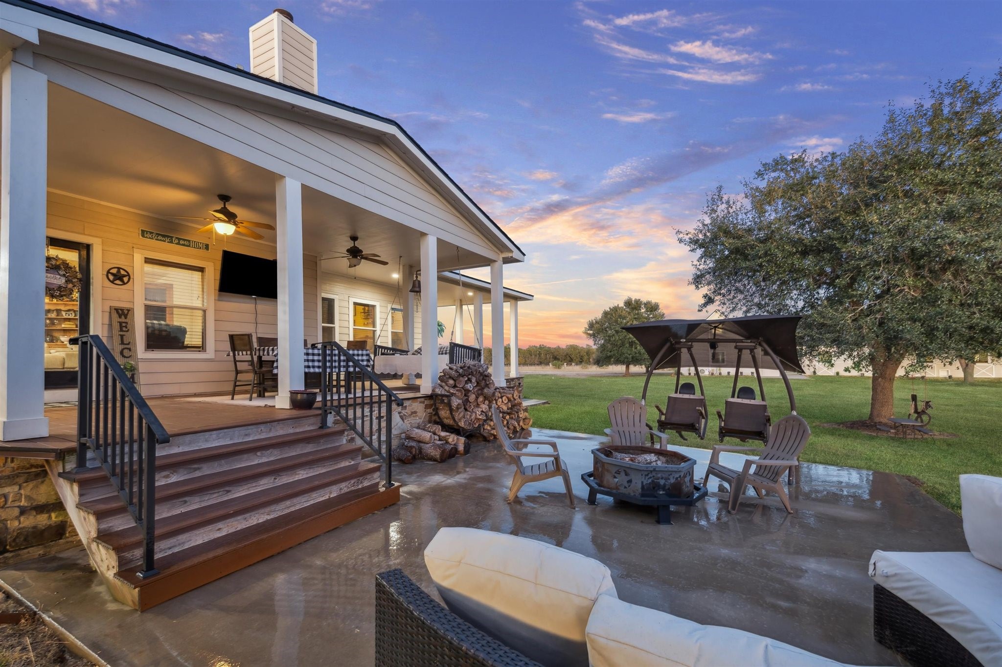 40570 Wildlife Run Hempstead, TX 77445 - Photo 30 of 43 This inviting backyard retreat features a charming firepit lounge surrounded by Adirondack chairs and swings, with a neat stack of firewood ready for the season. The covered porch offers fans, soft lighting, and a cozy dining nook perfect for winding down at sunset or gathering with guests beneath the wide Texas skies.