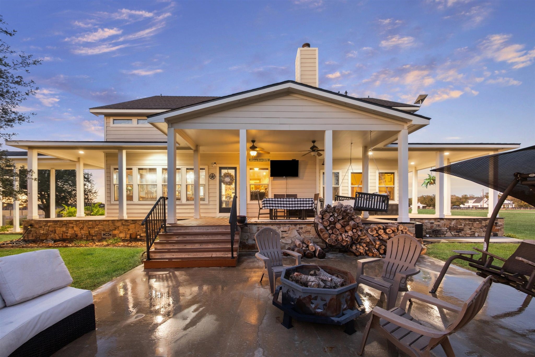 40570 Wildlife Run Hempstead, TX 77445 - Photo 31 of 43 As dusk sets in, the full view of the wraparound porch glows with warmth and welcome. With dual staircases, porch swings, and stacked firewood for the firepit, this backyard is perfectly designed for entertaining or simply relaxing into the calm of a country evening.