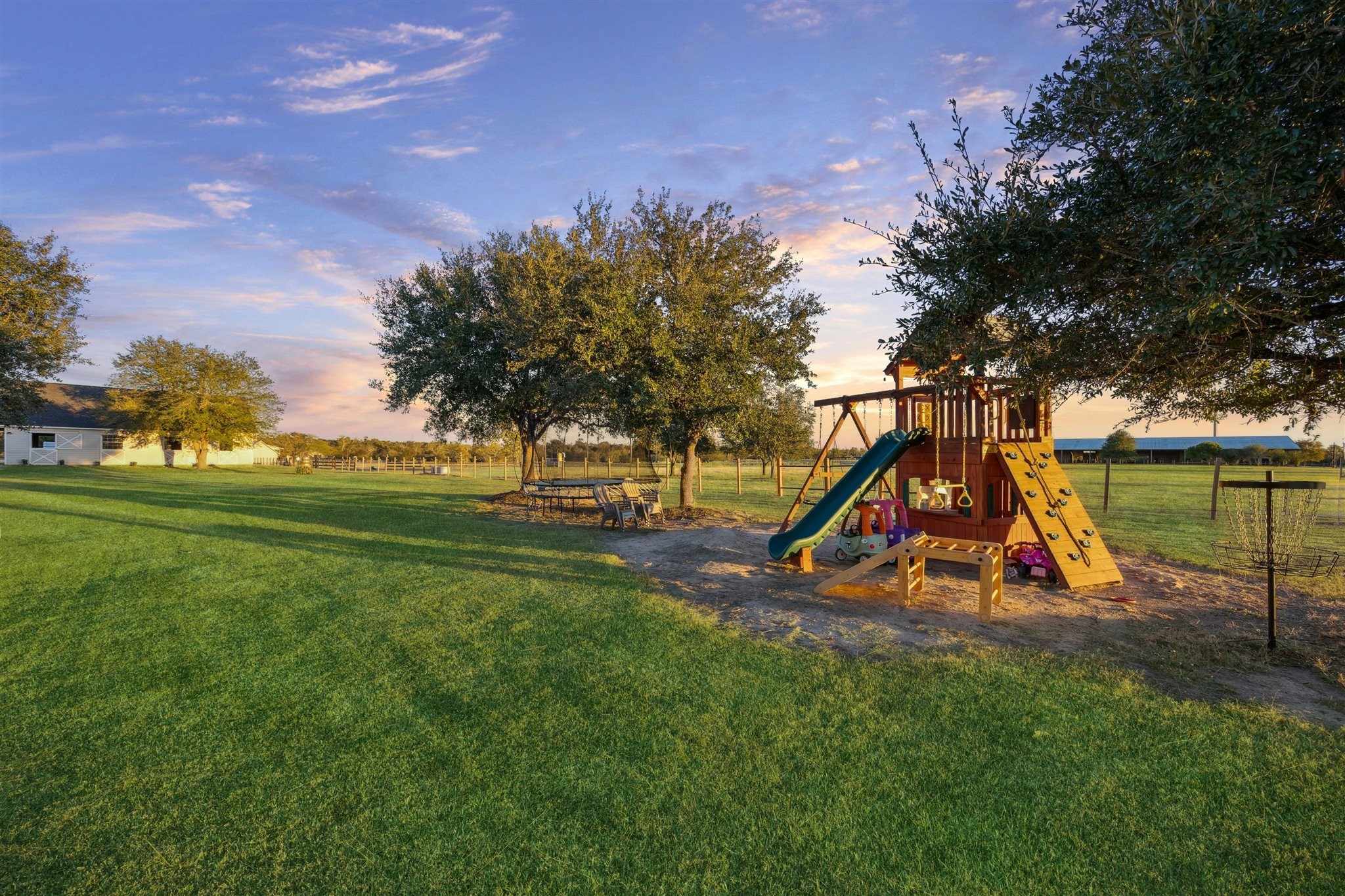 40570 Wildlife Run Hempstead, TX 77445 - Photo 34 of 43 Surrounded by open pasture and shaded by mature trees, this backyard playground is a dream for children. Featuring a wooden playset with rock wall, swings, slide, and monkey bars, plus a picnic table beneath the trees, it’s built for joyful afternoons and endless imagination, set on land that benefits from a wildlife exemption, blending play with purpose.