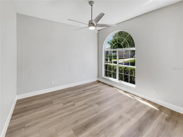 an empty room with wooden floor fan and windows
