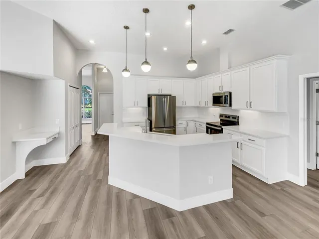 a kitchen with stainless steel appliances kitchen island granite countertop a stove a sink a refrigerator and white cabinets with wooden floor