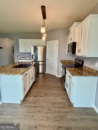 a kitchen with stainless steel appliances granite countertop a stove top oven a sink a refrigerator white cabinets and wooden floor