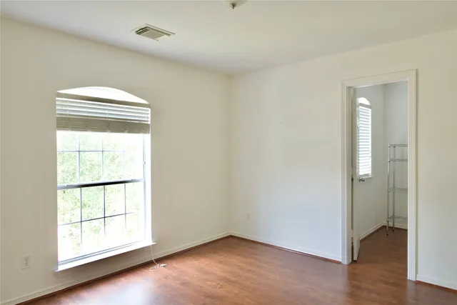 an empty room with wooden floor closet and windows