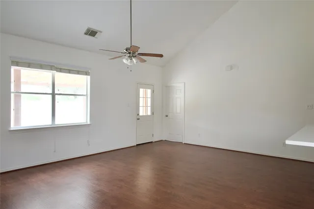 an empty room with wooden floor chandelier fan and windows