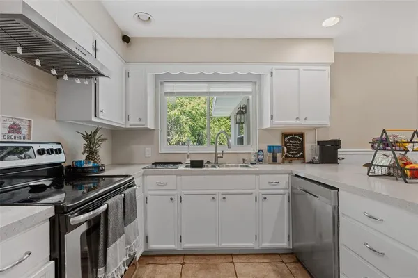 a kitchen with white cabinets appliances a sink and a window