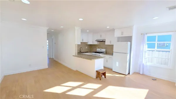 a large kitchen with stainless steel appliances granite countertop a stove a sink a refrigerator and white cabinets with wooden floor