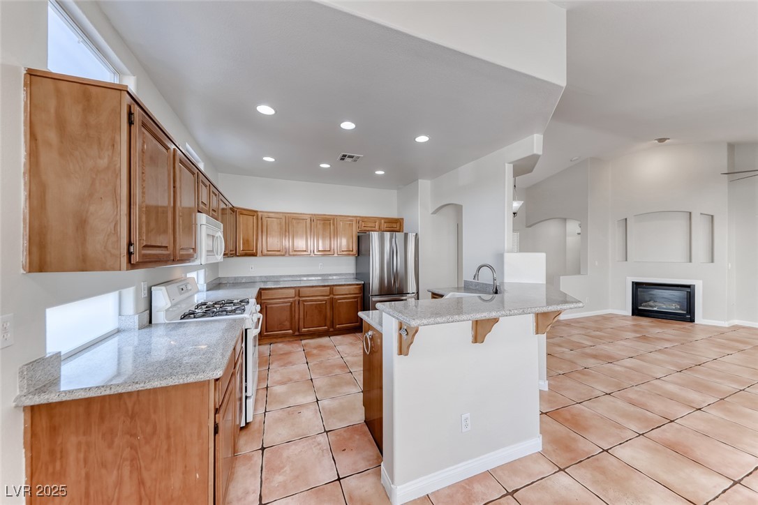 698 Magic Cove Court Boulder City, NV 89005 - Photo 23 of 41 Kitchen featuring a kitchen bar, white appliances, light tile patterned flooring, recessed lighting, and light stone counters