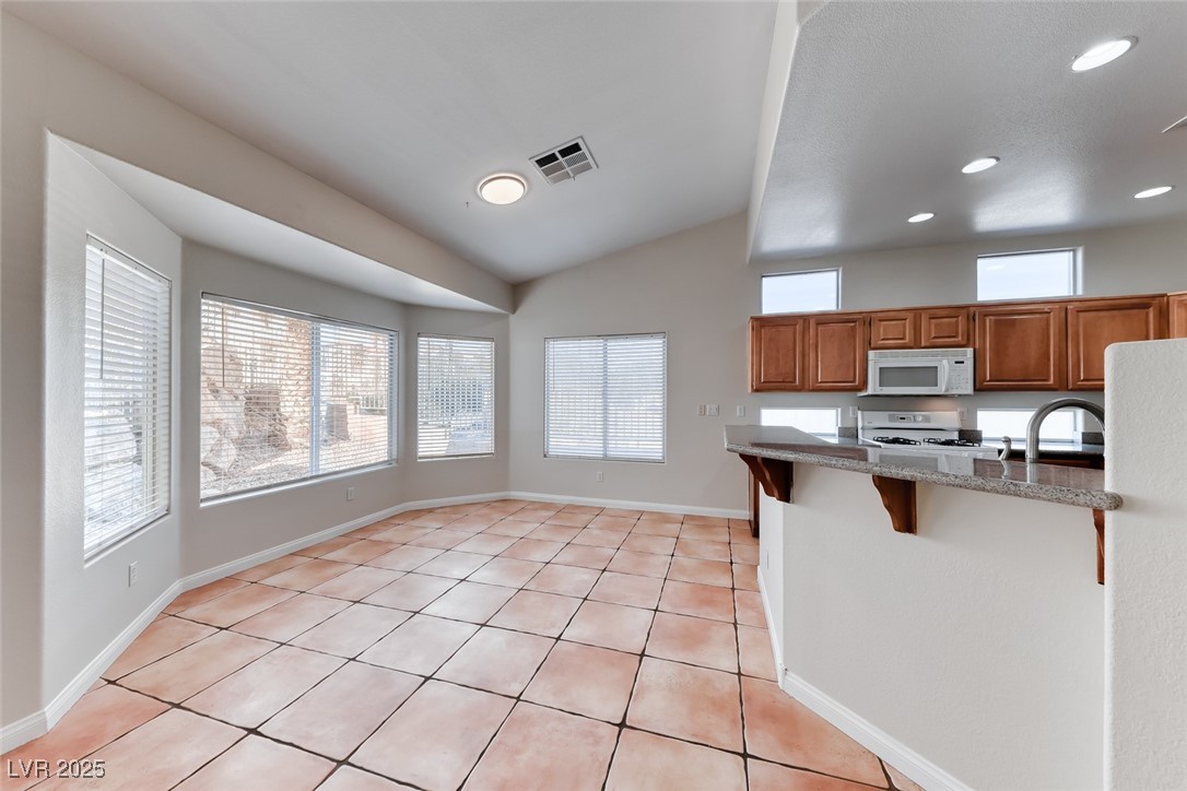 698 Magic Cove Court Boulder City, NV 89005 - Photo 29 of 41 Kitchen with brown cabinetry, a breakfast bar area, plenty of natural light, light tile patterned flooring, and vaulted ceiling