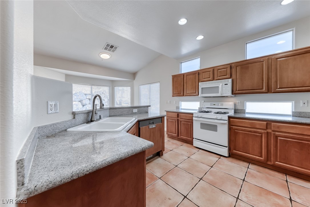 698 Magic Cove Court Boulder City, NV 89005 - Photo 30 of 41 Kitchen with white appliances, brown cabinets, light tile patterned floors, vaulted ceiling, and light stone counters