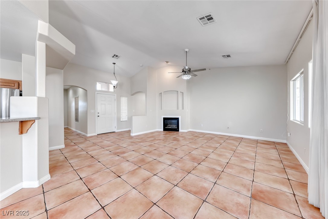 698 Magic Cove Court Boulder City, NV 89005 - Photo 34 of 41 Unfurnished living room with light tile patterned floors, a glass covered fireplace, vaulted ceiling, ceiling fan, and healthy amount of natural light
