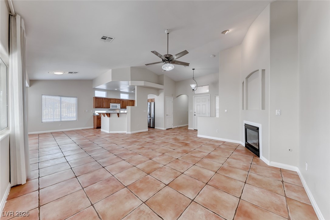 698 Magic Cove Court Boulder City, NV 89005 - Photo 4 of 41 Unfurnished living room with light tile patterned floors, arched walkways, a glass covered fireplace, ceiling fan, and lofted ceiling