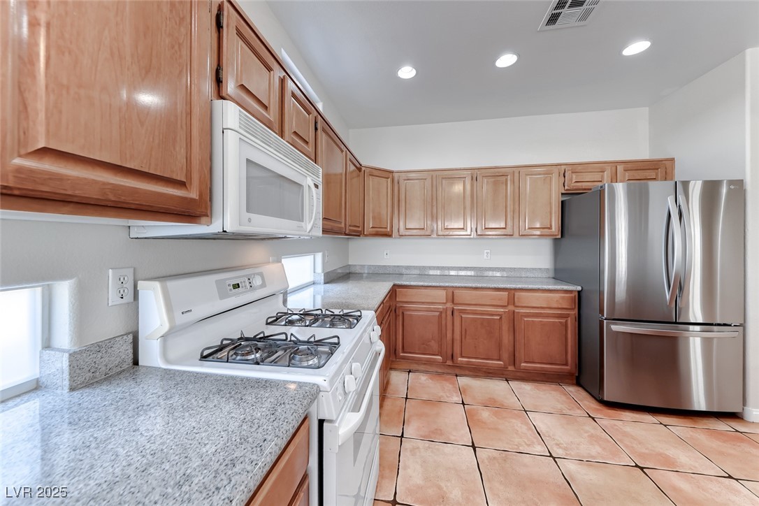698 Magic Cove Court Boulder City, NV 89005 - Photo 5 of 41 Kitchen with white appliances, light tile patterned floors, recessed lighting, light stone countertops, and brown cabinets
