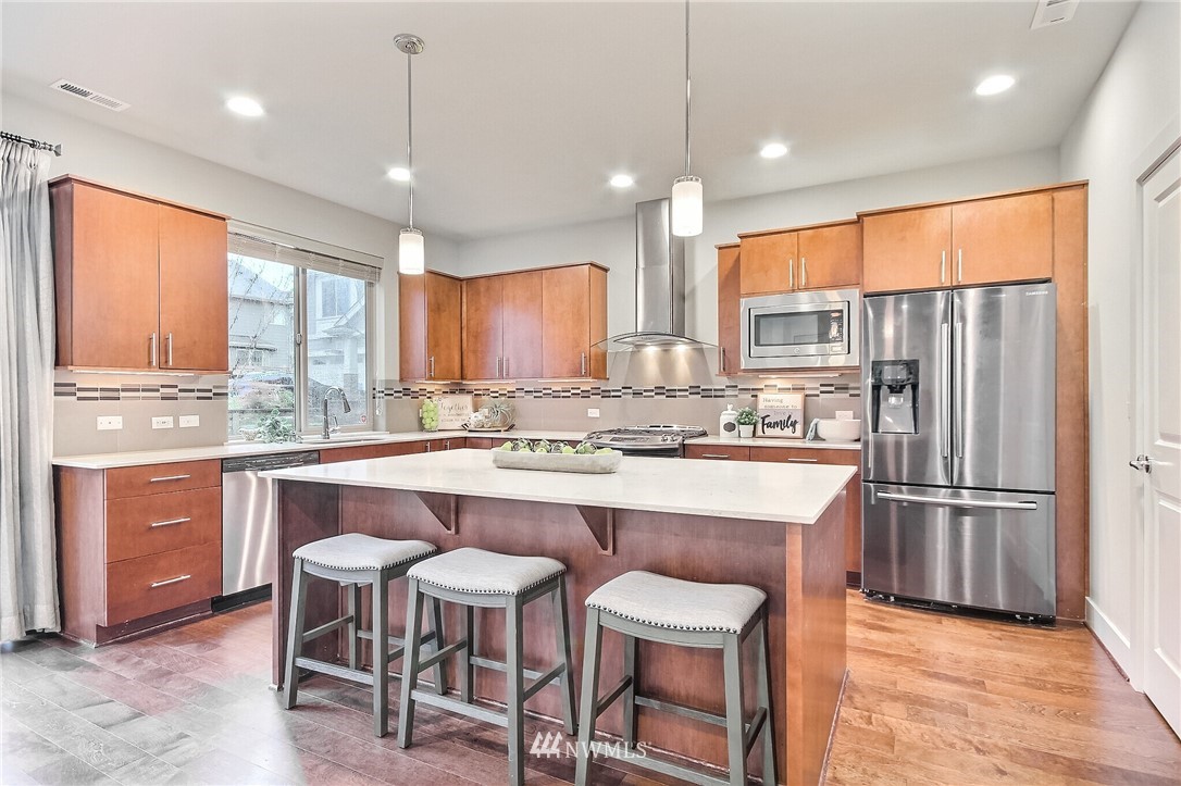 5113 Northeast 11th Place Renton, WA 98059 - Photo 13 of 40 a kitchen with kitchen island granite countertop wooden cabinets a refrigerator a stove a island and chairs with wooden floor