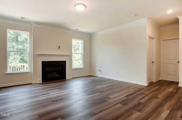 an empty room with wooden floor fireplace and windows