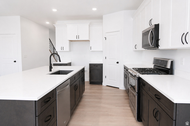 1004 West Paramount Cove South, Unit 315 Ogden, UT 84405 - Photo 11 of 42 Modern kitchen featuring a large island with an undermount sink and matte black faucet, stainless steel appliances, white upper cabinetry, dark wood-finish base cabinetry, and recessed lighting