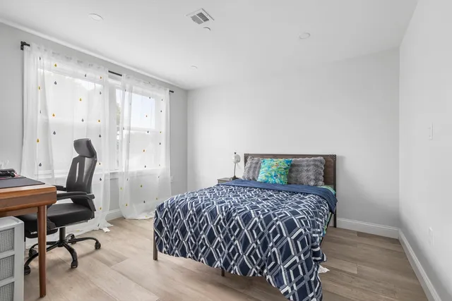 a bedroom with a bed a desk and chair with wooden floor