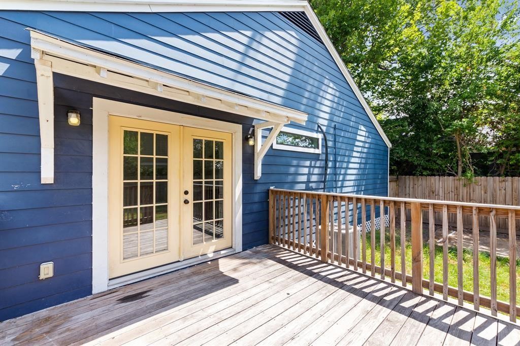 1305 Idylwild Street Houston, TX 77009 - Photo 18 of 31 This photo showcases a charming outdoor deck attached to a blue house. It features double French doors, a wooden railing, and a small overhang. The area is well-lit and opens to a grassy backyard, ideal for relaxation or entertaining.