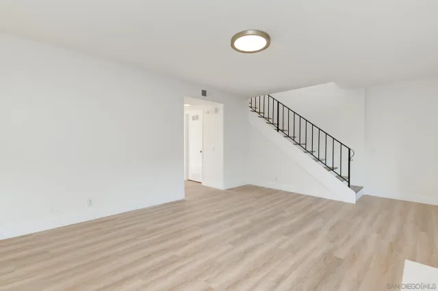 a view of an empty room with wooden floor and stairs