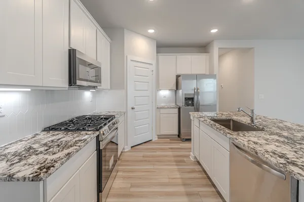 a kitchen with granite countertop kitchen island stainless steel appliances a stove refrigerator sink and cabinets