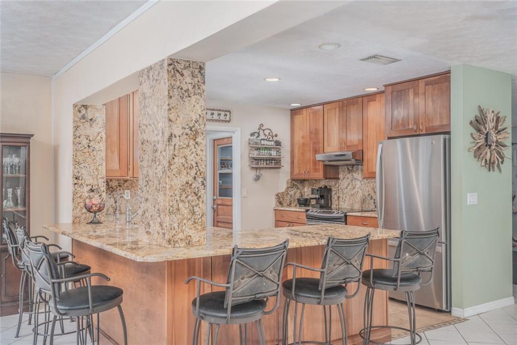 1128 Northwest Fork Road Stuart, FL 34994 - Photo 7 of 23 a kitchen with stainless steel appliances kitchen island granite countertop a refrigerator and a wooden cabinets