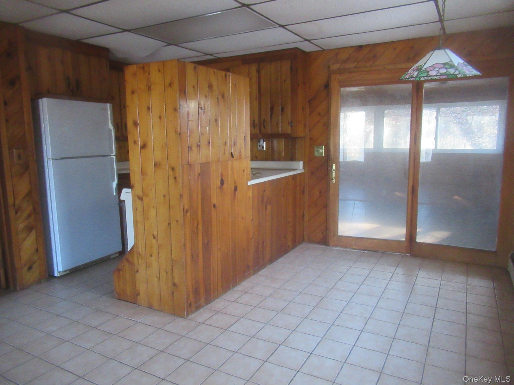 270 Bucks Hollow Road Mahopac, NY 10541 - Photo 4 of 11 Kitchen featuring freestanding refrigerator, a paneled ceiling, wooden walls, brown cabinetry, and light tile patterned floors