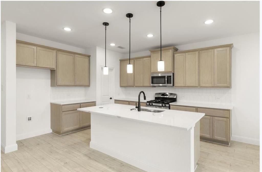 2902 Hanscom Street Forney, TX 75126 - Photo 7 of 28 Kitchen featuring stainless steel appliances, a center island with sink, light wood-style flooring, pendant lighting, and light stone countertops