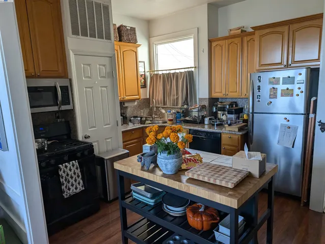 a living room with stainless steel appliances furniture a rug and a kitchen view