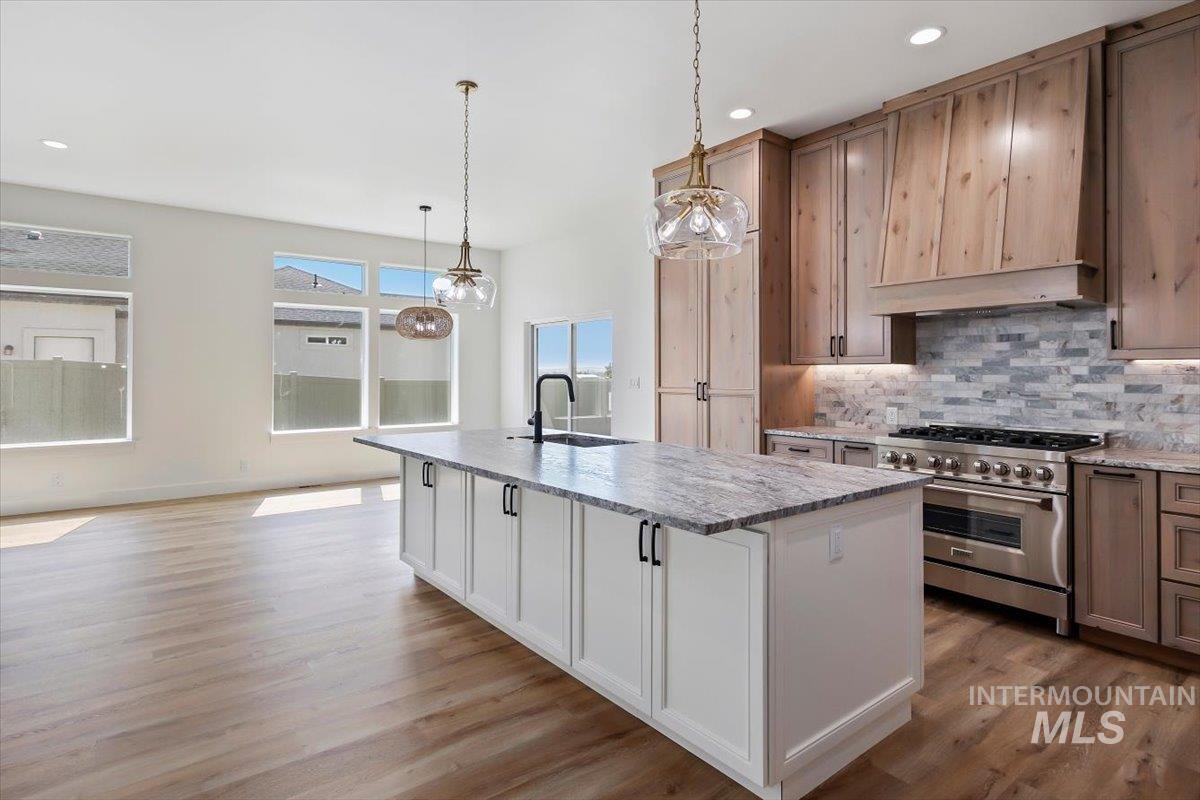 563 Moonstone Road Kimberly, ID 83341 - Photo 15 of 48 Gourmet kitchen with natural wood cabinetry, stainless steel range, light-toned wood-finish flooring, a large island with a stone countertop, and modern pendant lighting