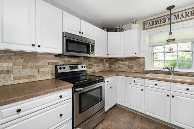 a kitchen with granite countertop white cabinets appliances a sink and a window