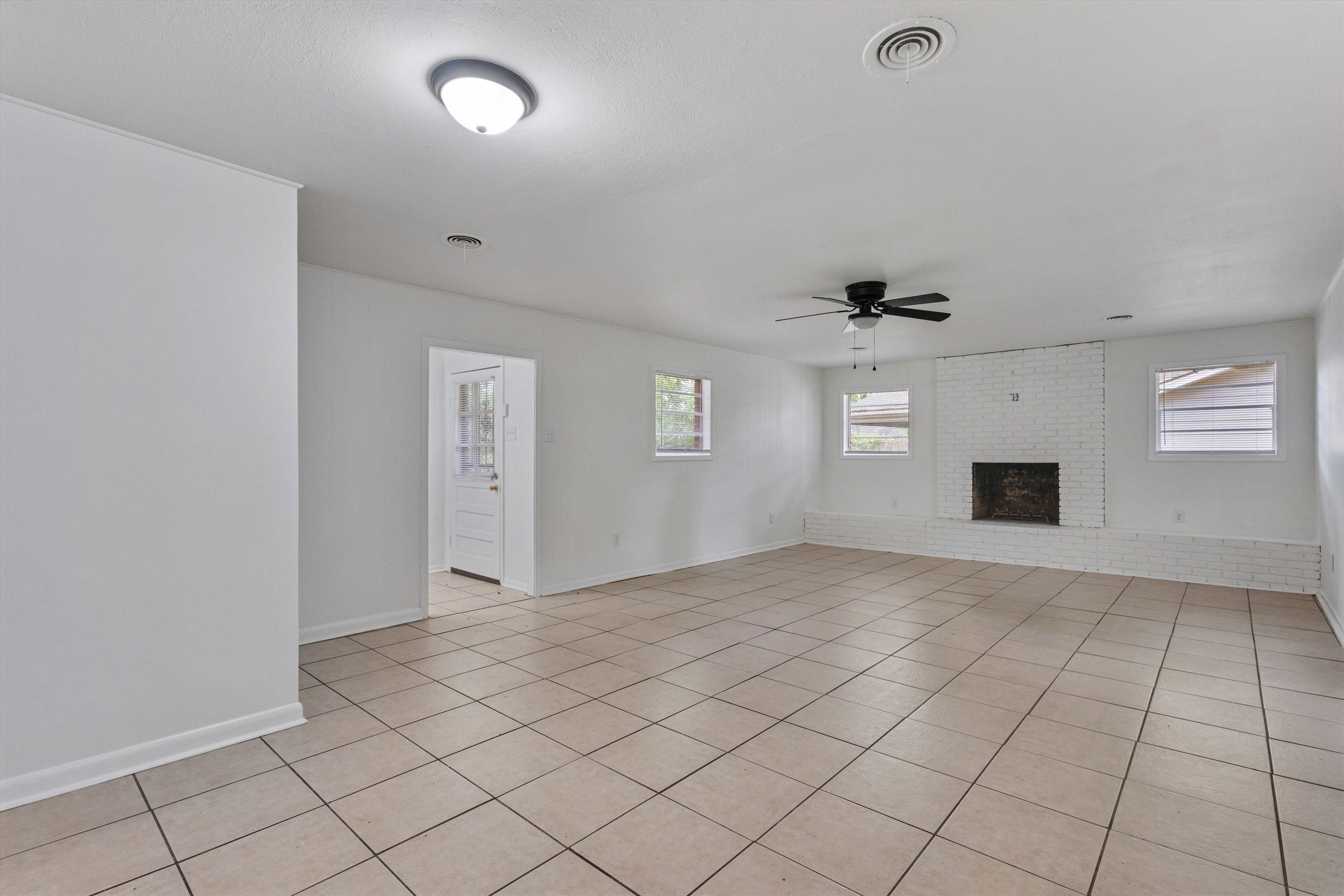 4565 Verne Road Memphis, TN 38117 - Photo 7 of 18 Spacious living area featuring neutral-toned floor tiling, a painted brick fireplace, white walls, and multiple windows
