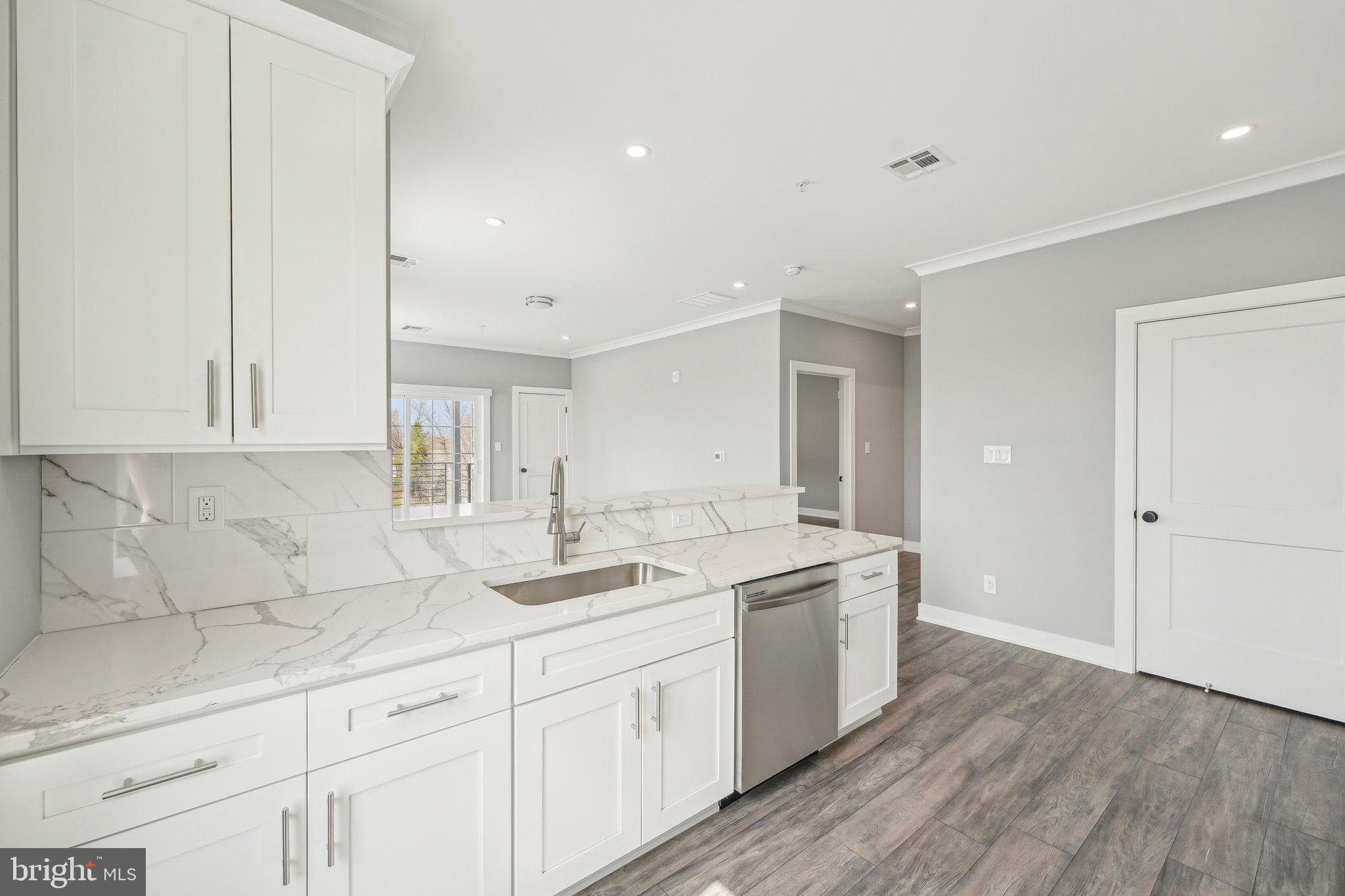2421 Bristol Road, Unit 1B203 Warrington, PA 18976 - Photo 6 of 50 a kitchen with a sink dishwasher and white cabinets with wooden floor