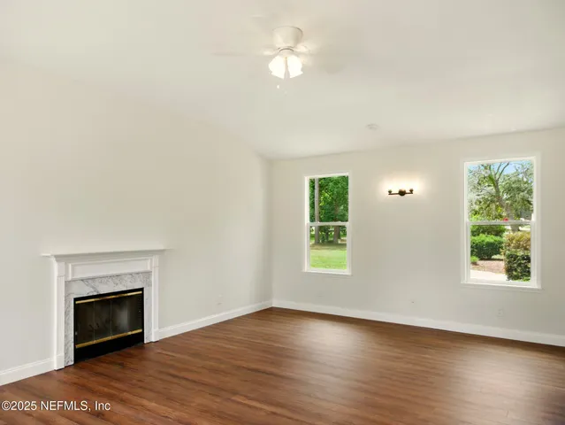 an empty room with wooden floor chandelier fan and windows