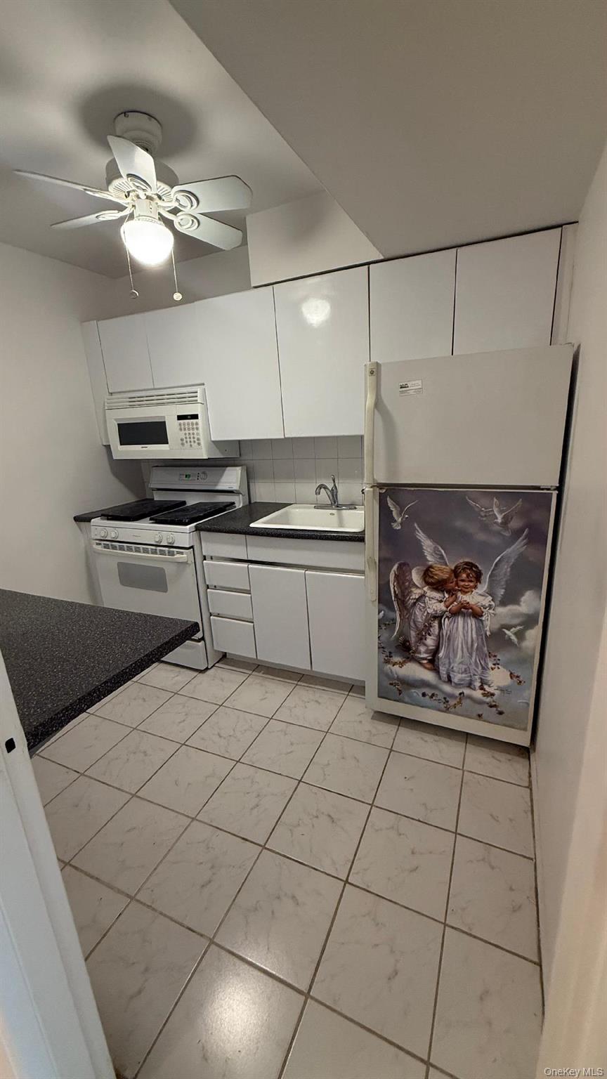 88-25 155th Avenue, Unit 4G Queens, NY 11414 - Photo 3 of 8 Kitchen with white cabinets, white appliances, ceiling fan, dark countertops, and decorative backsplash
