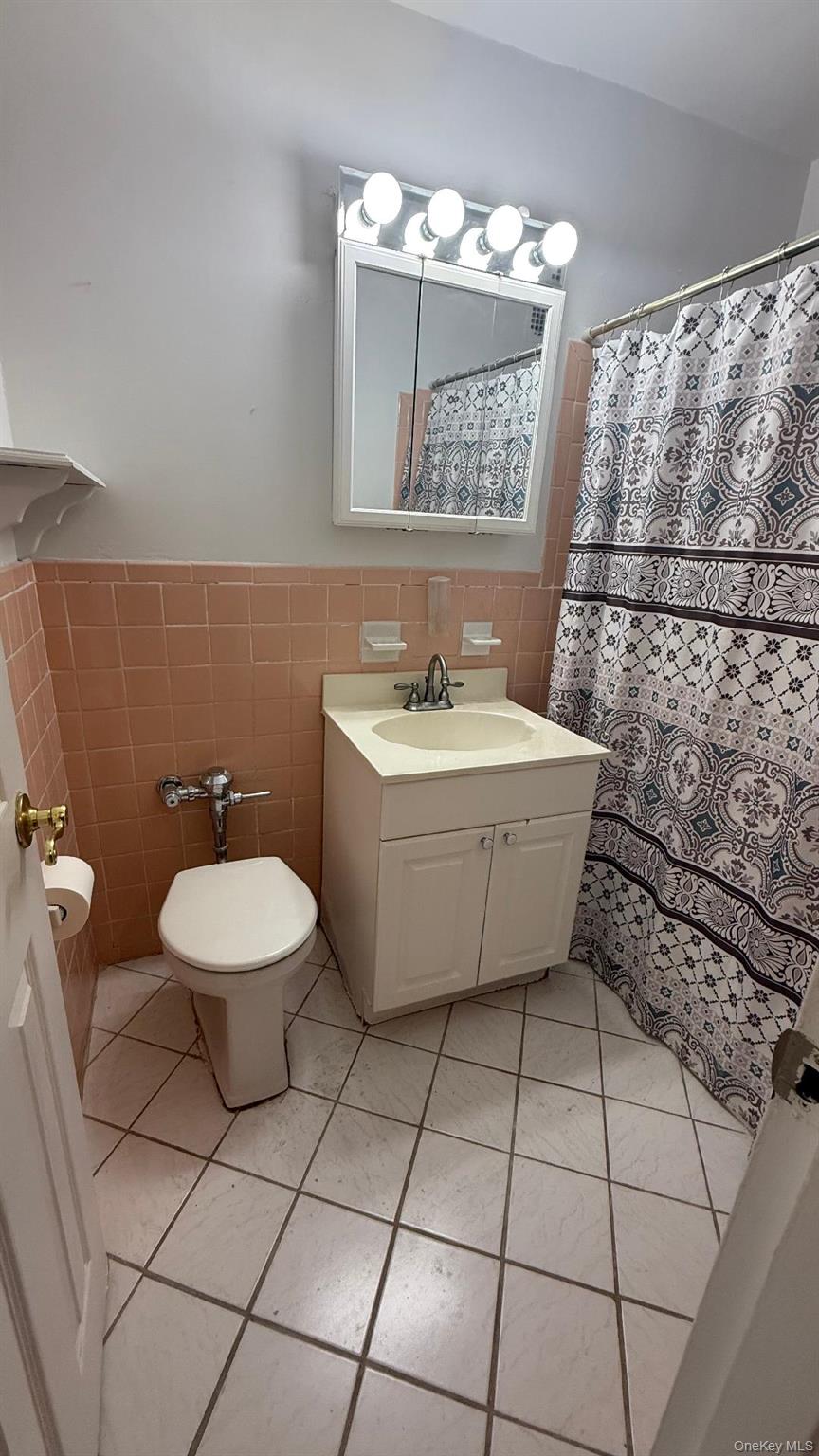 88-25 155th Avenue, Unit 4G Queens, NY 11414 - Photo 4 of 8 Bathroom featuring tile walls, vanity, light tile patterned floors, a wainscoted wall, and a shower with curtain